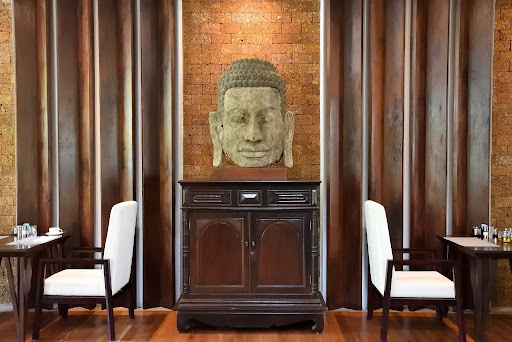 Carved stone Buddha head displayed on a wooden cabinet between two armchairs
