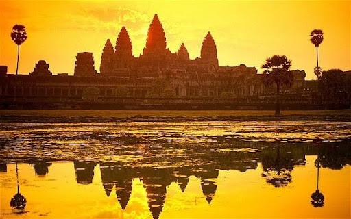 Silhouette of Angkor Wat's towers reflected in water at sunset