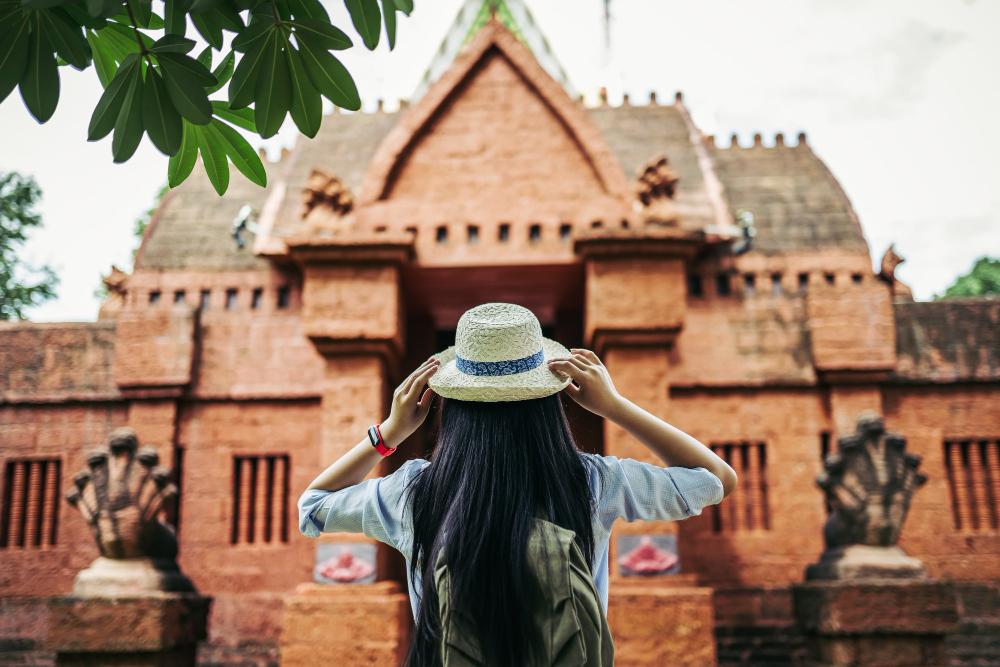 Traveller in a sun hat standing before the gateway of a red laterite temple