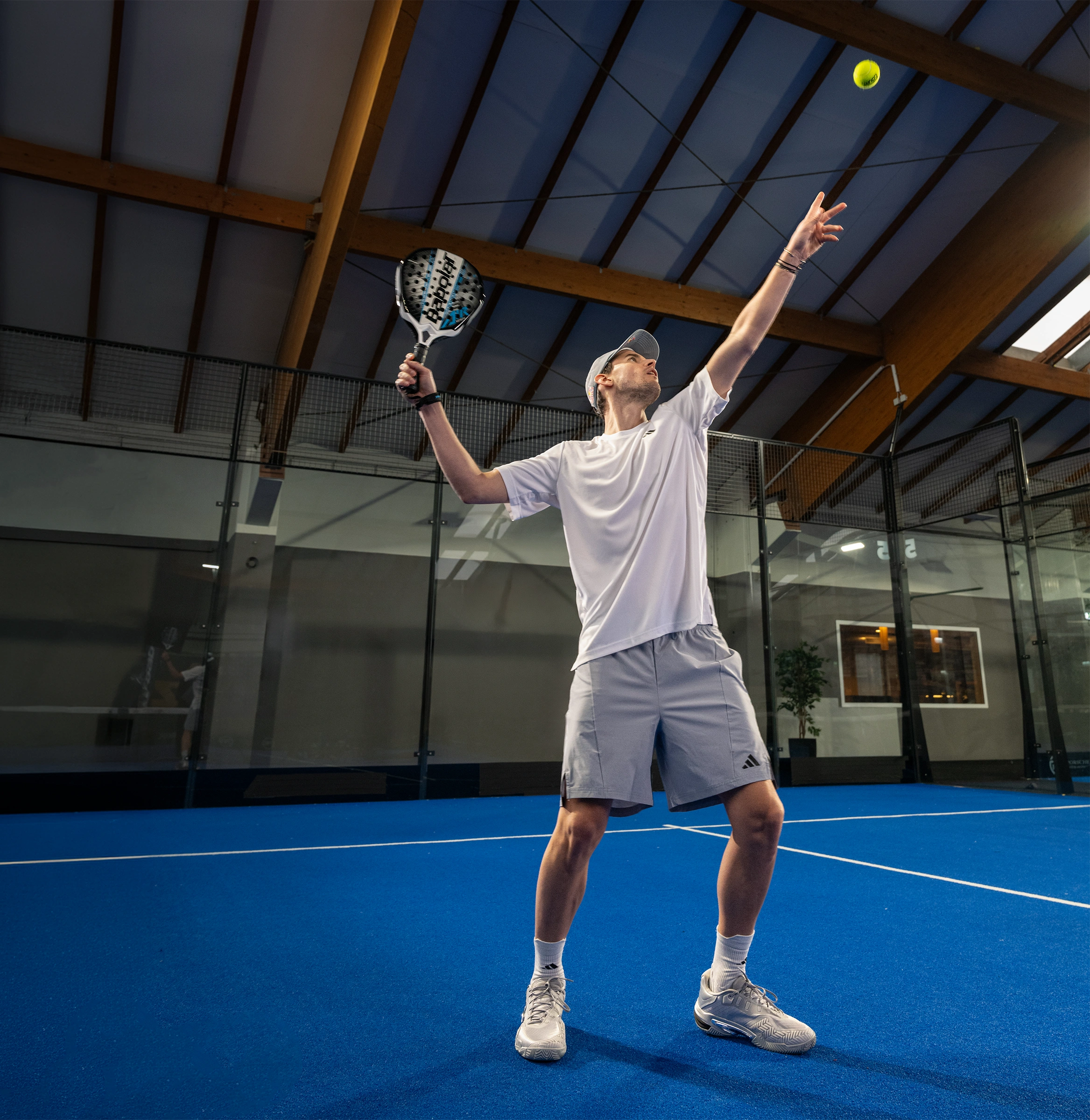 Dominic Thiem spielt in weißem Tennis Outfit in einer Halle Tennis