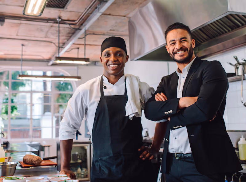 Chef standing next to restaurant owner smiling and standing inside commercial kitchen