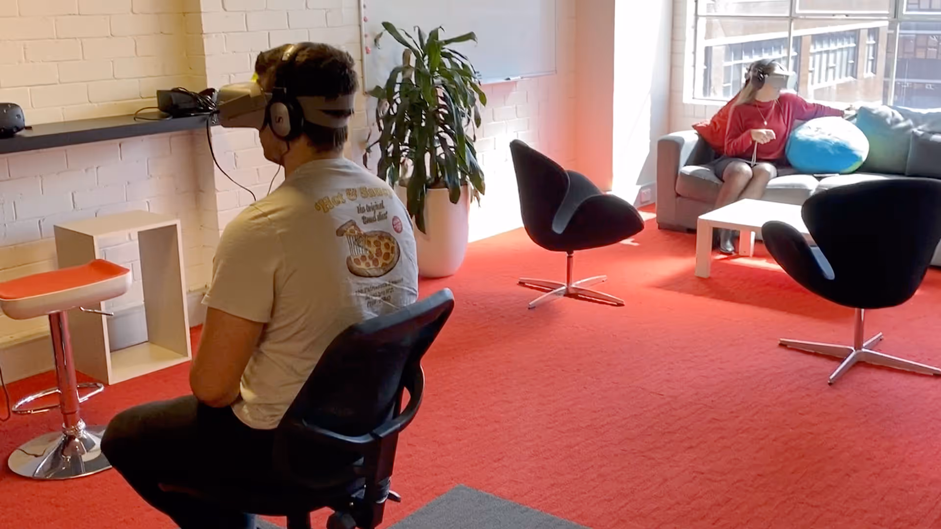 a man wearing virtual reality headset sitting in a room with a man in a chair