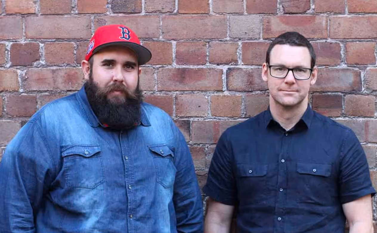 two men standing in front of a brick wall