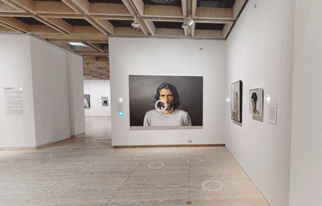 Matterport tour view of a gallery wall hung with framed portraits, including a large photographic self-portrait.