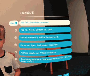 VR screen showing a "Tongue" exercise checklist with a Play button and a completed list of oral exercises, with a child visible in the corner.