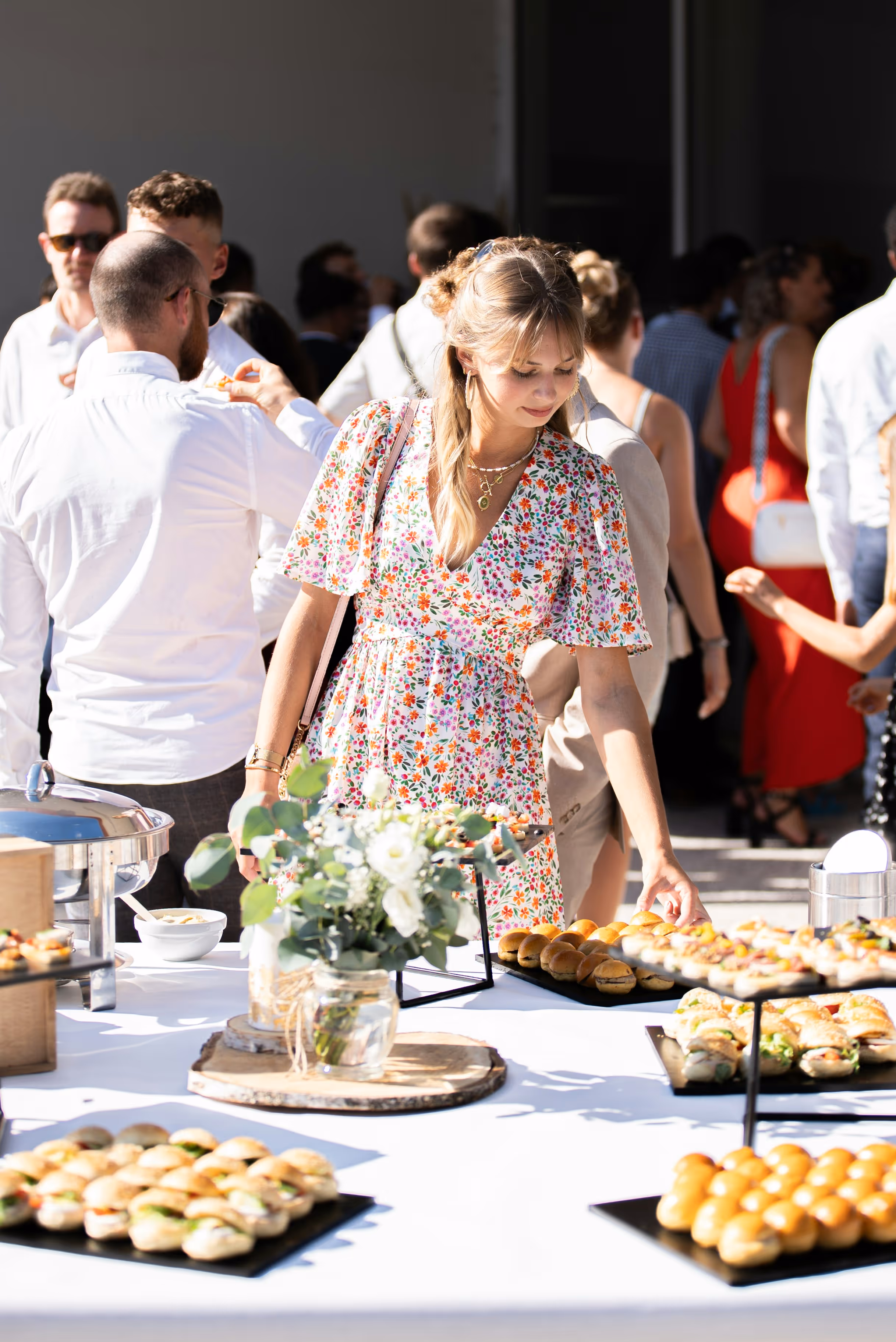 Woman in floral dress selecting food from a buffet table at a social outdoor event.
