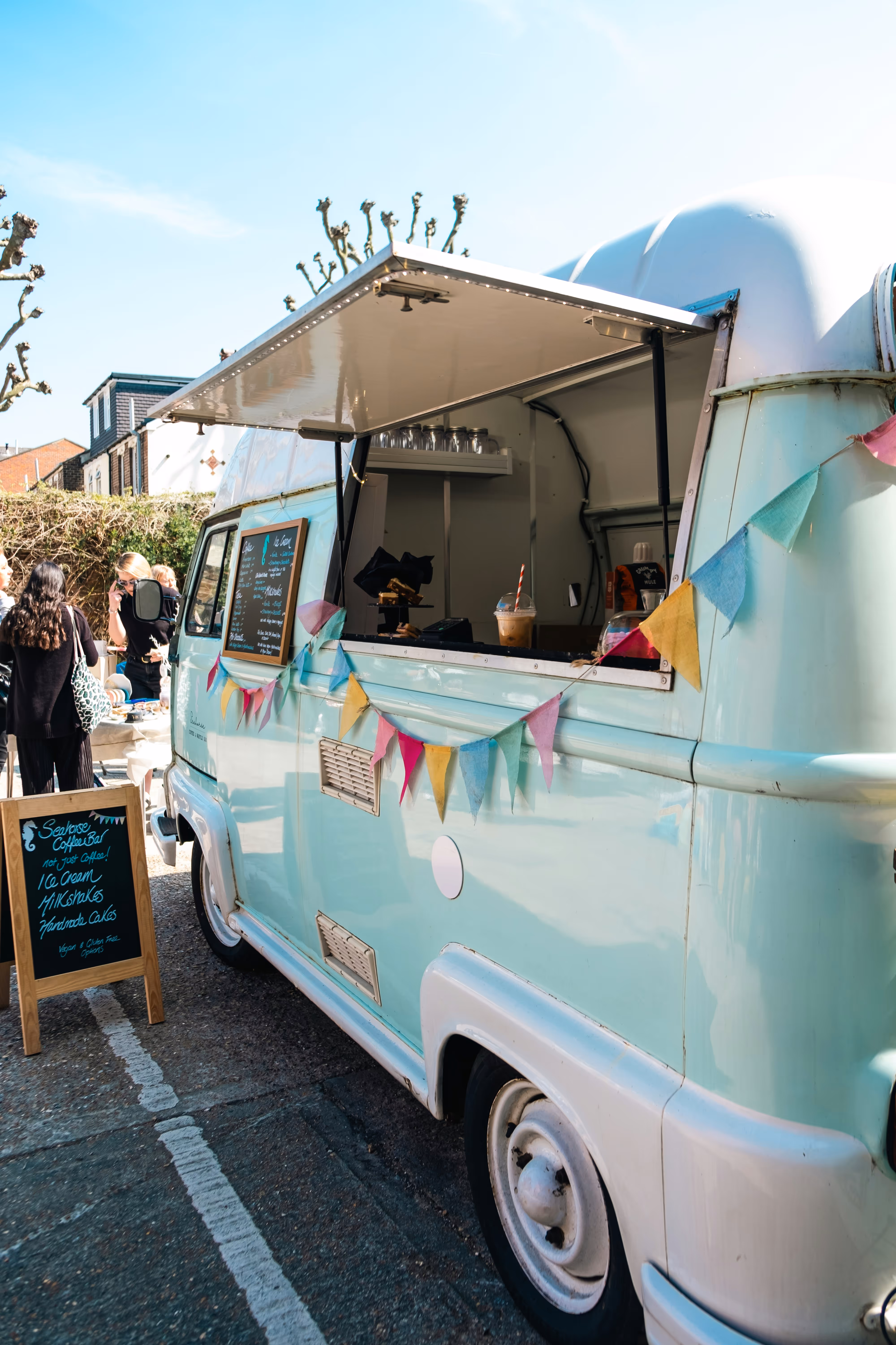 Aqua vintage food truck with colorful bunting and a menu board, serving customers outdoors.