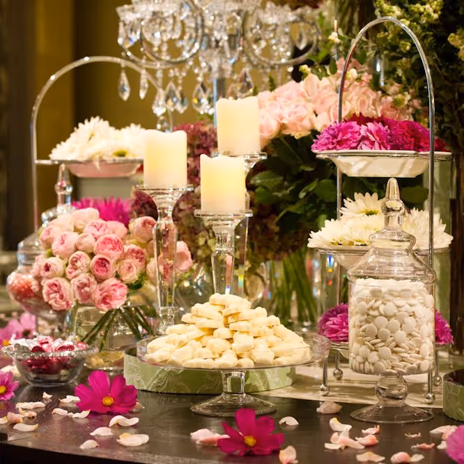 Decorative table with candles, pink roses, white flowers, candies, and scattered petals at an event.