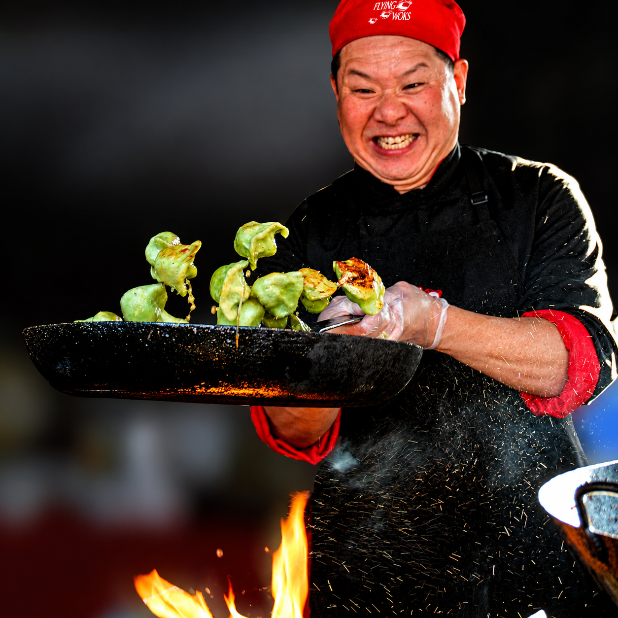 Chef tossing green dumplings in a flaming wok with intense focus and energy.
