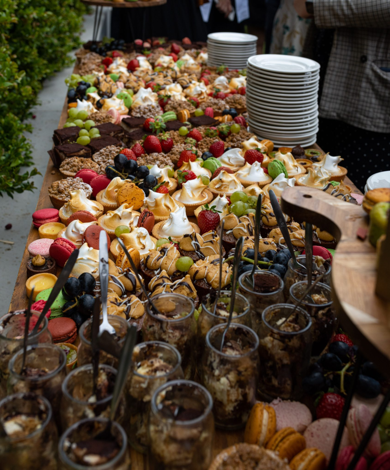 Table with assorted desserts including cupcakes, macarons, fruit, and dessert jars with spoons.