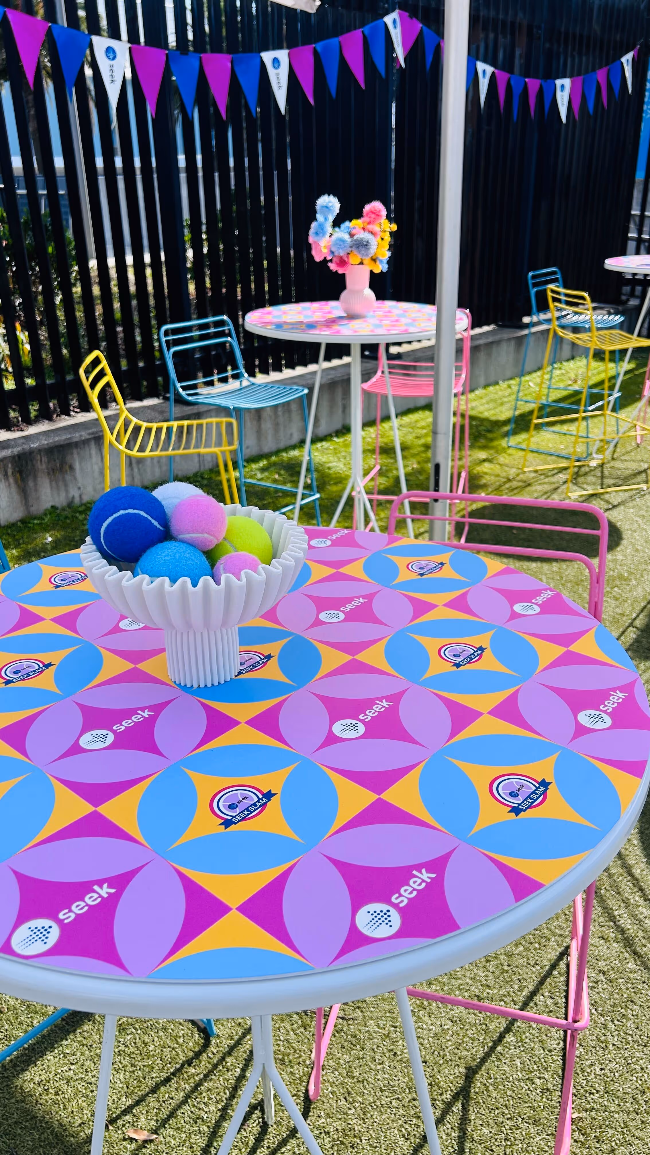 Colorful outdoor tables with Seek Slam logos, vibrant chairs, and bowls of colorful tennis balls.