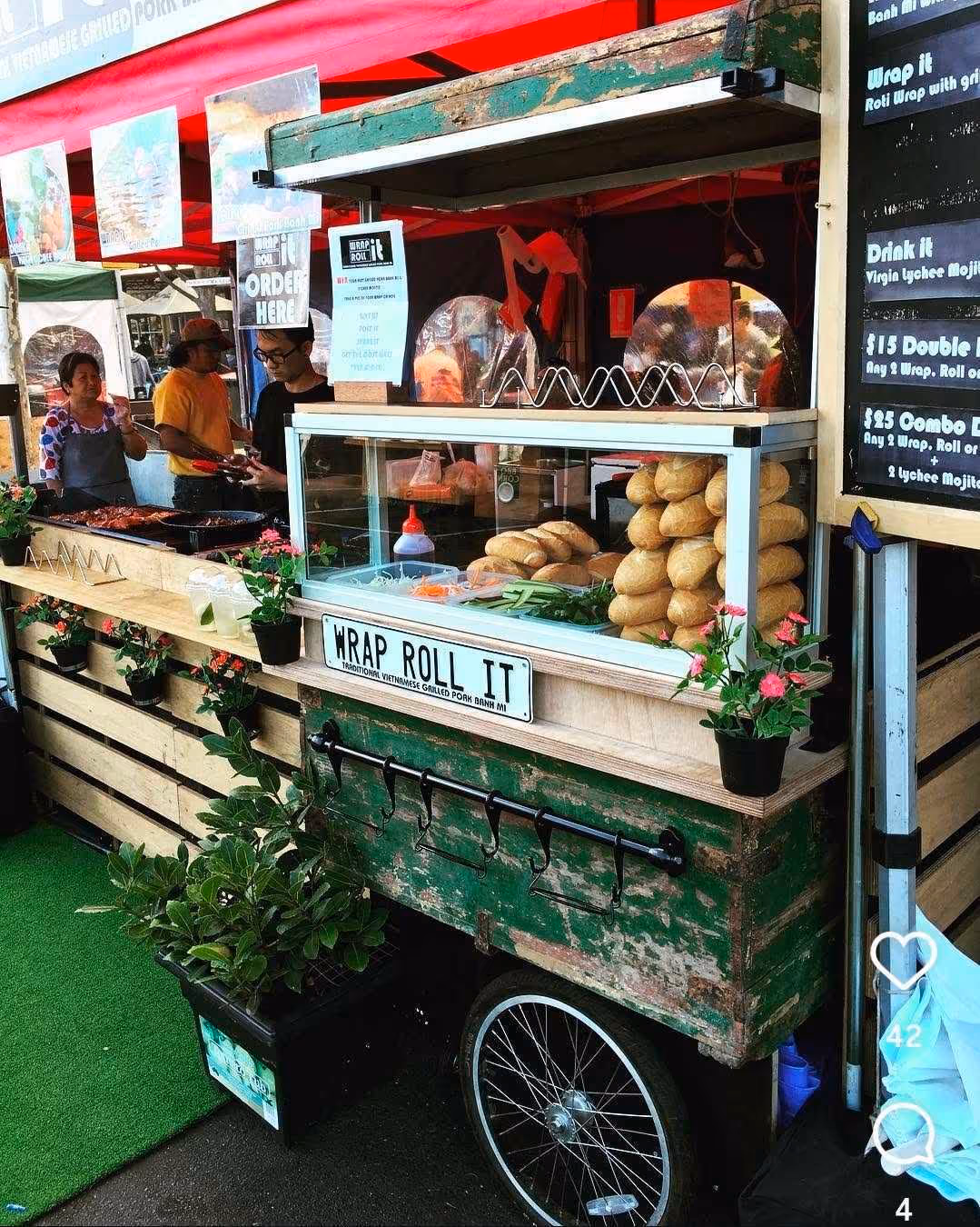Vintage food cart labeled Wrap Roll It with Vietnamese baguettes and ingredients displayed behind glass.