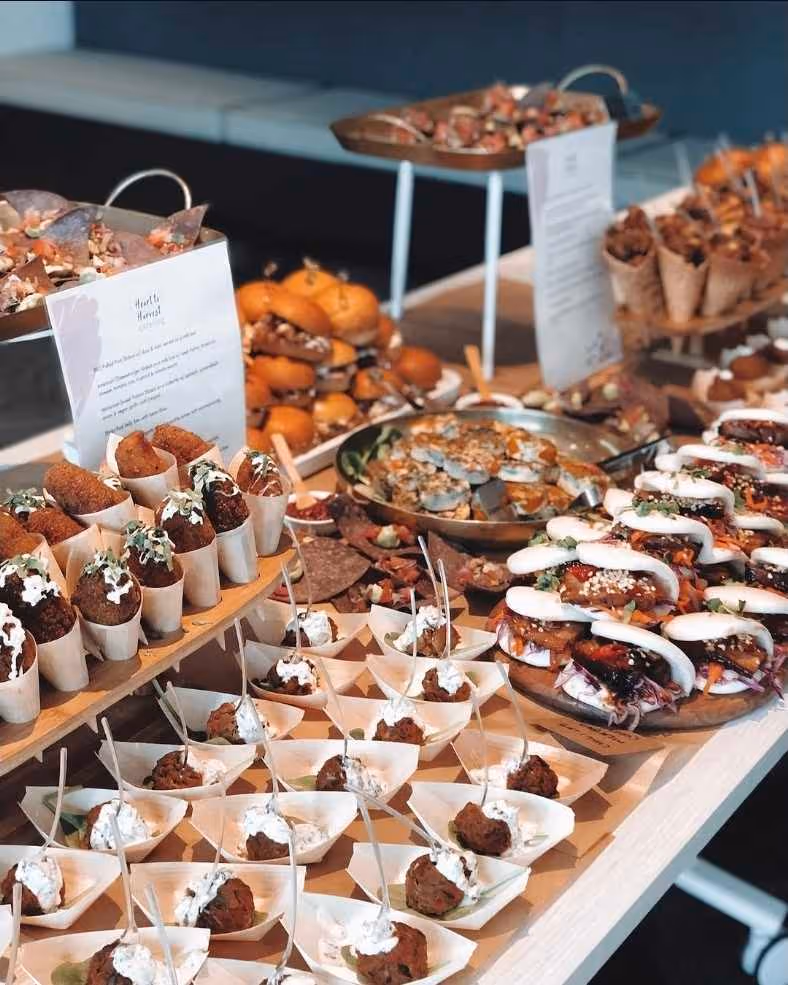 Table with assorted appetizers including sliders, meatballs, bao buns, and finger foods in paper servings.