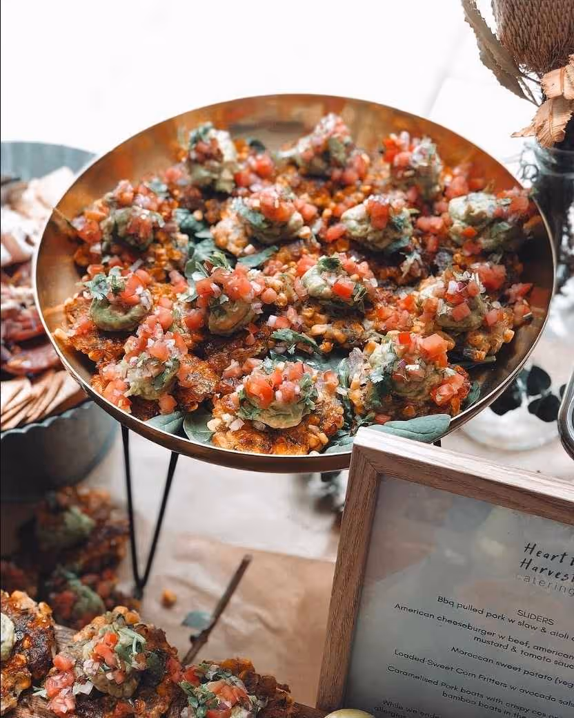 Plate of sweet corn fritters topped with guacamole, diced tomatoes, and herbs on a table.