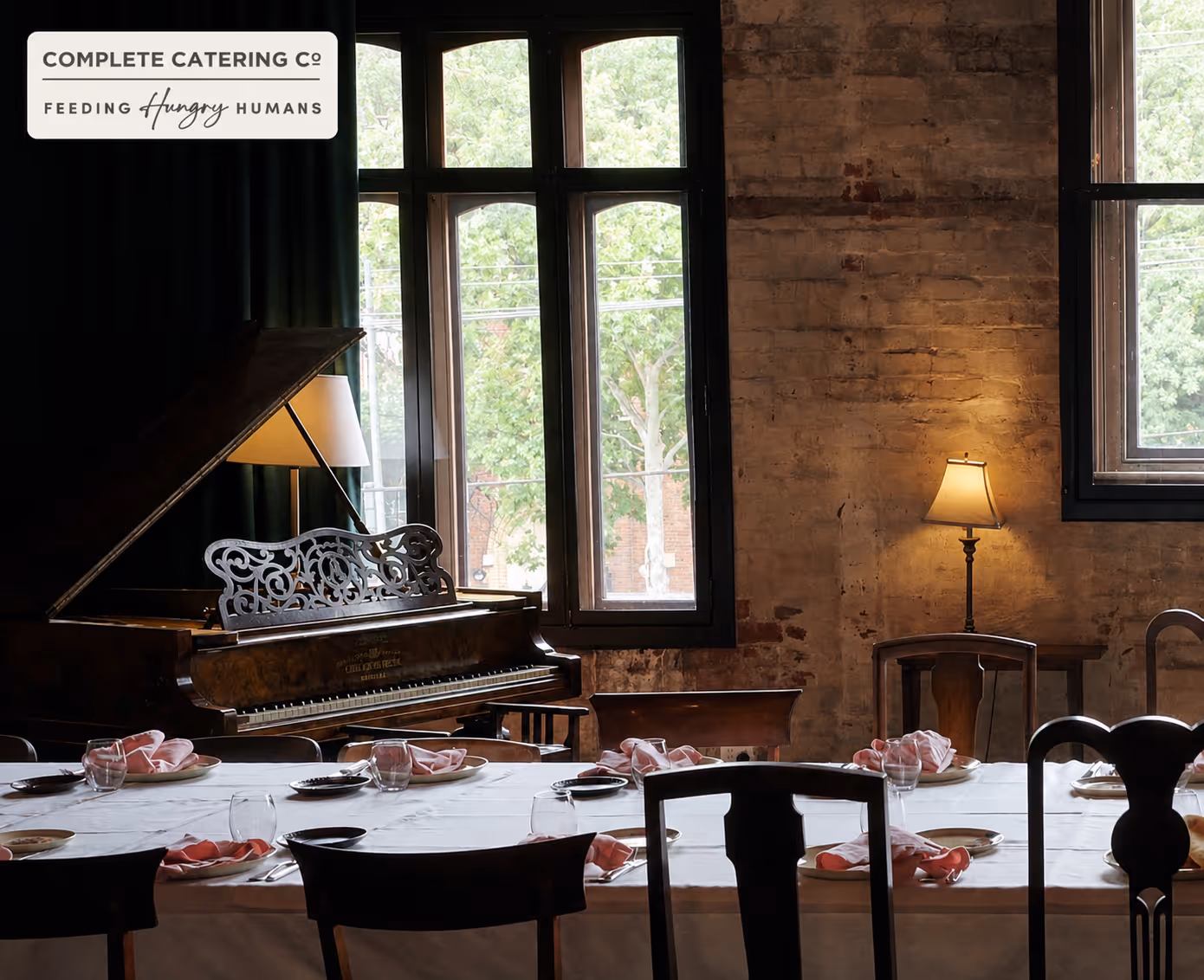 Dining room with a set table, grand piano, and windows letting in natural light.