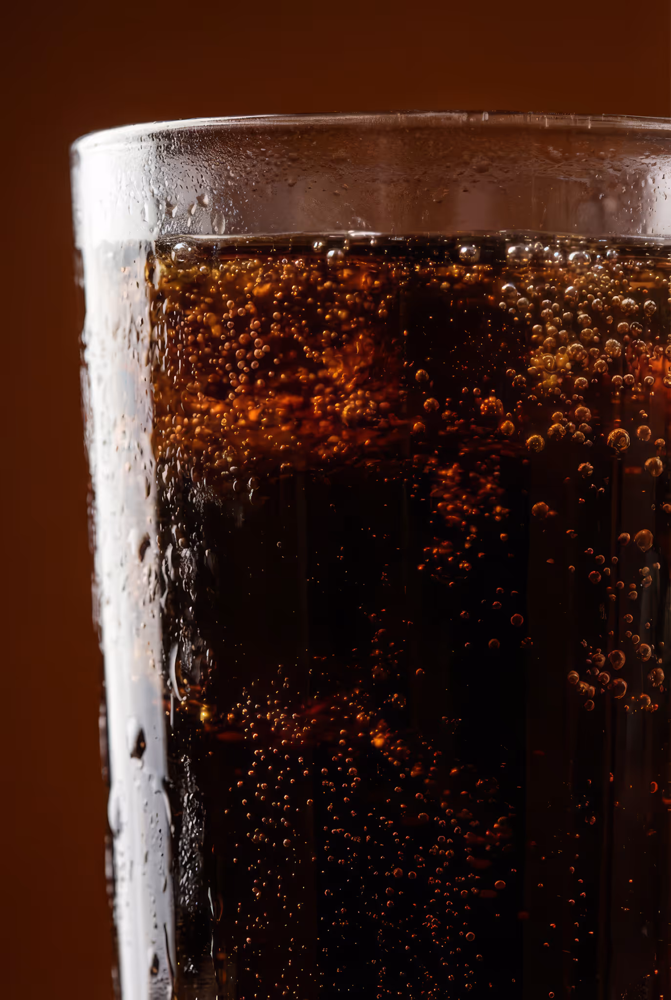 Close-up of a glass filled with dark soda with visible bubbles and condensation on the glass.