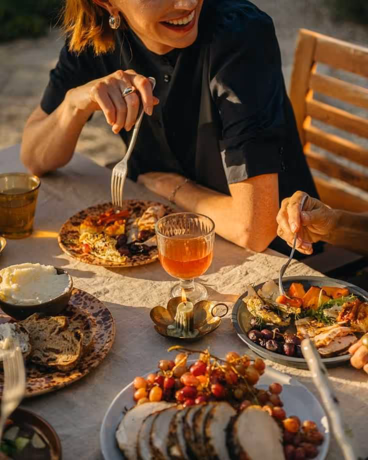 Four hands clinking glasses of Aperol Spritz above orange flowers at outdoor table under umbrella.
