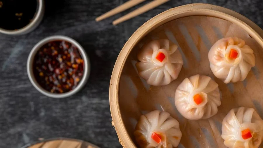 Bamboo steamer with dumplings and a small bowl of chilli oil.