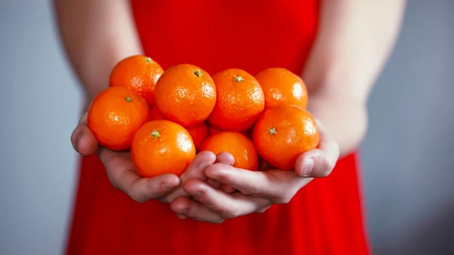 Woman in a red dress holding a bunch of mandarins.