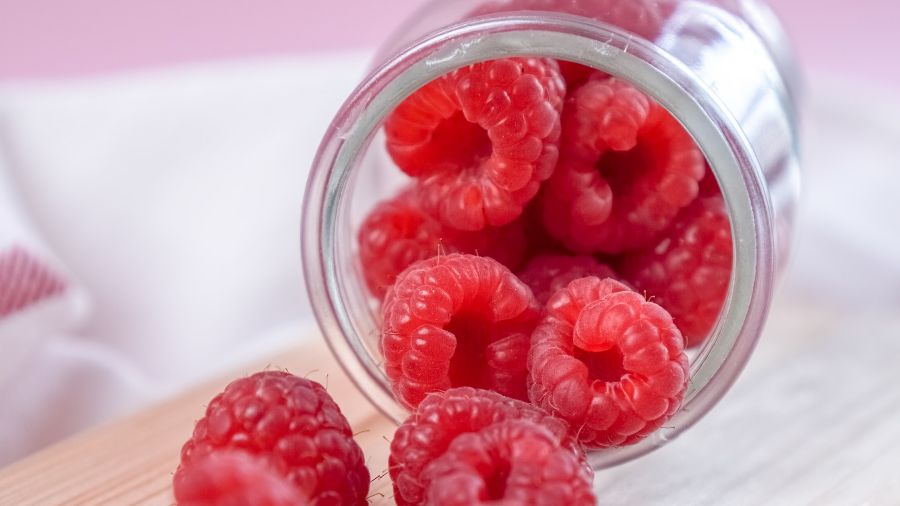 Raspberries falling out of a tipped over jar.