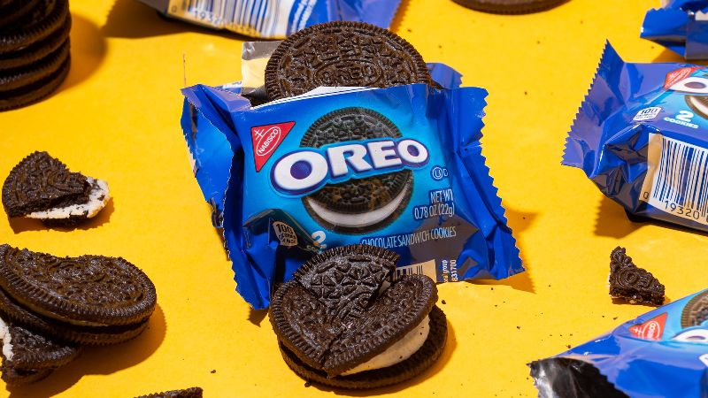 Oreo wrappers and cookies, some broken, on a yellow backdrop.