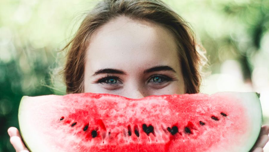 A woman holding up a quarter of a watermelon in front of her face like it's her smile.