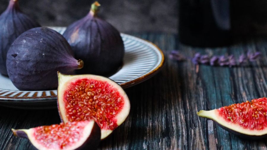 Plate with three full figs on a table with a few sliced figs on it.