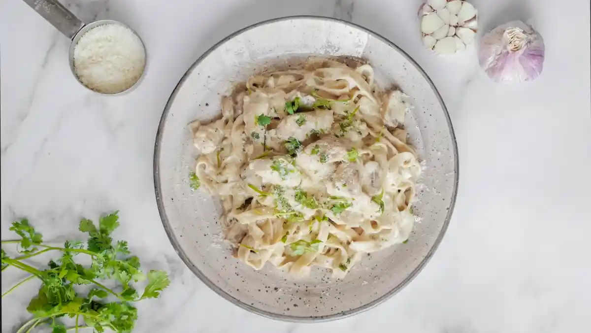 Bowl of pasta on a marble table with garlic, coriander and parmesan cheese.