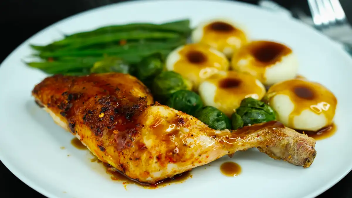 Roast chicken, potatoes and greens with gravy on a white plate.