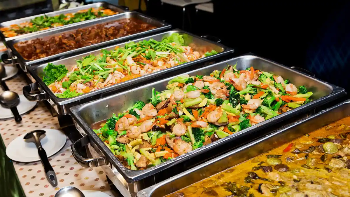 A table with five bain-maries at a buffet that are full of food.