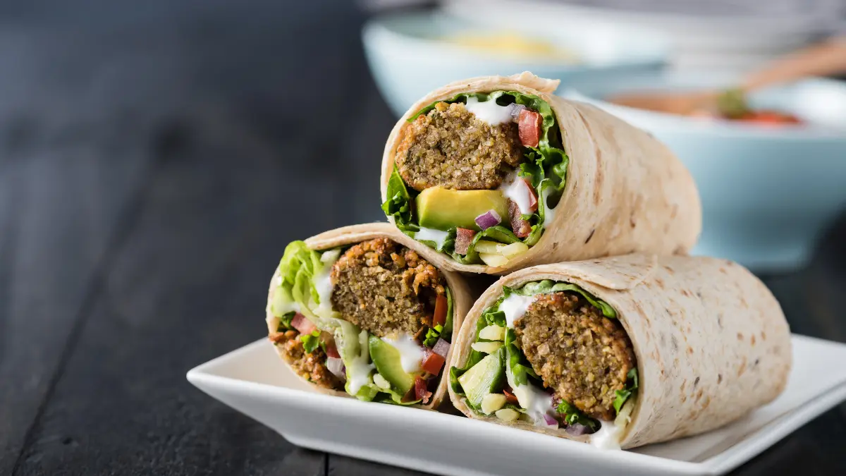 Three falafel wraps sitting on a plate.