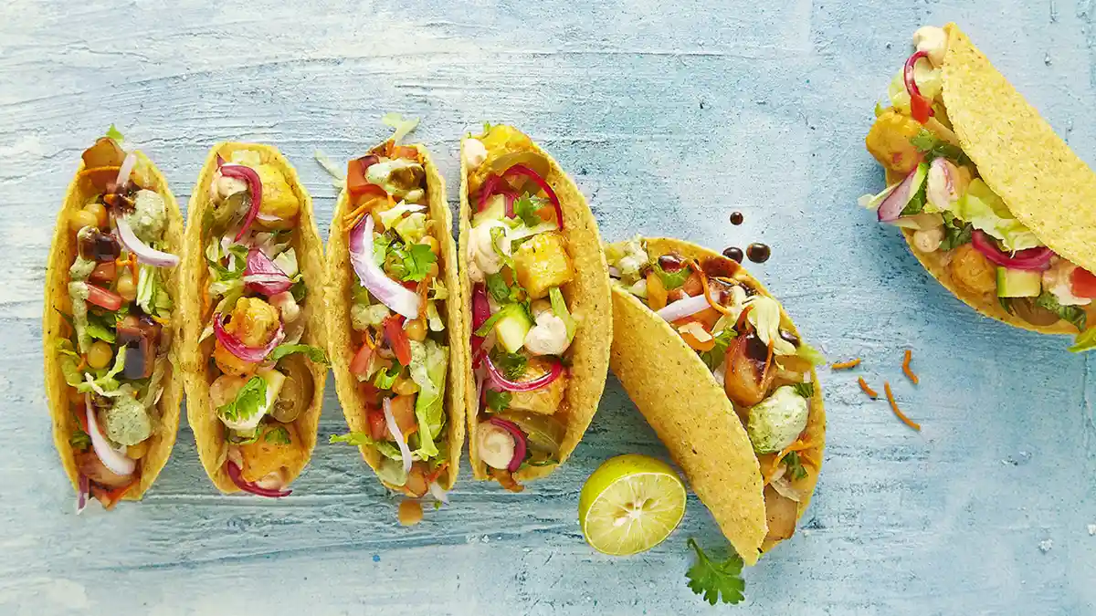 Six hard-shell tacos on a blue table with a lime.
