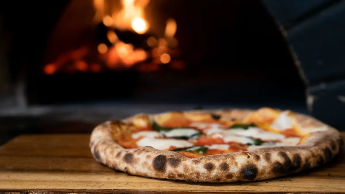 A fresh pizza coming out of a wood fired pizza oven.