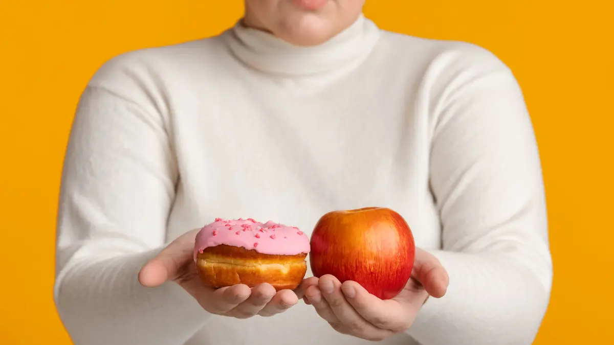 A woman holding an apple in one hand and a donut in the other.