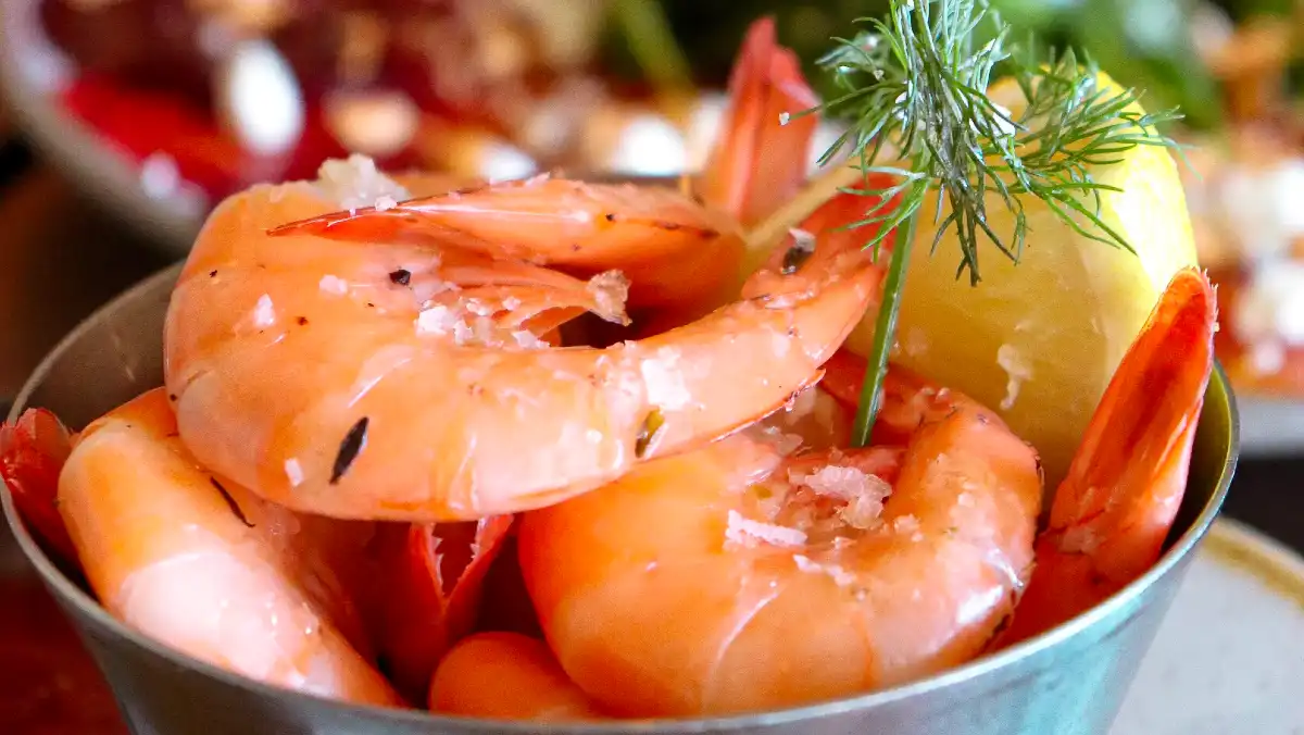 A metal bucket of prawns with lemon and dill.