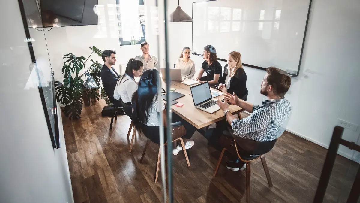 A group of people sitting around a wodden table having a meeting.
