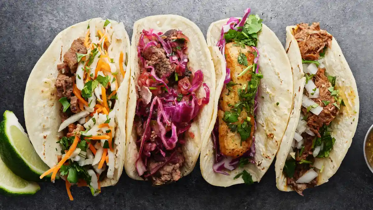 Four soft-shell tacos with various fillings, including pulled pork and grilled fish.