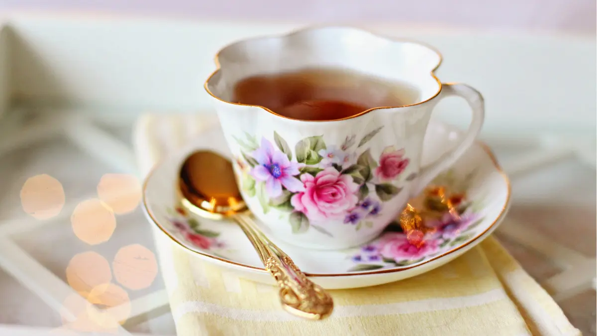 A tea cup with a golden spoon sitting on a folded yellow napkin.