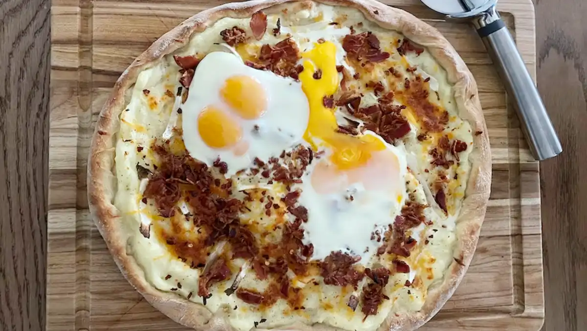 A breakfast pizza with bacon, eggs and cheese, on a wooden cutting board.