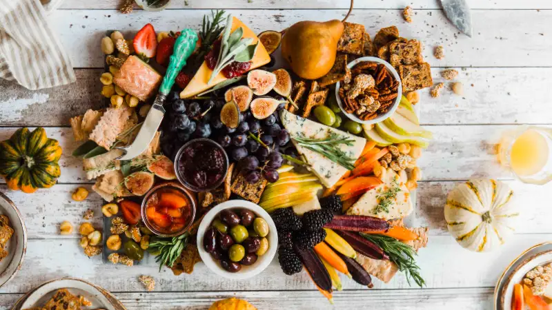 Wooden table with a grazing board including cheese, grapes, olives and biscuits.