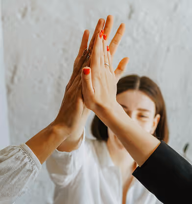 Three people giving a group high-five with a smiling woman in the background.