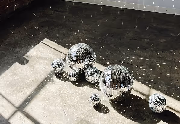 Multiple disco balls of varying sizes on a sunlit floor casting scattered light reflections.