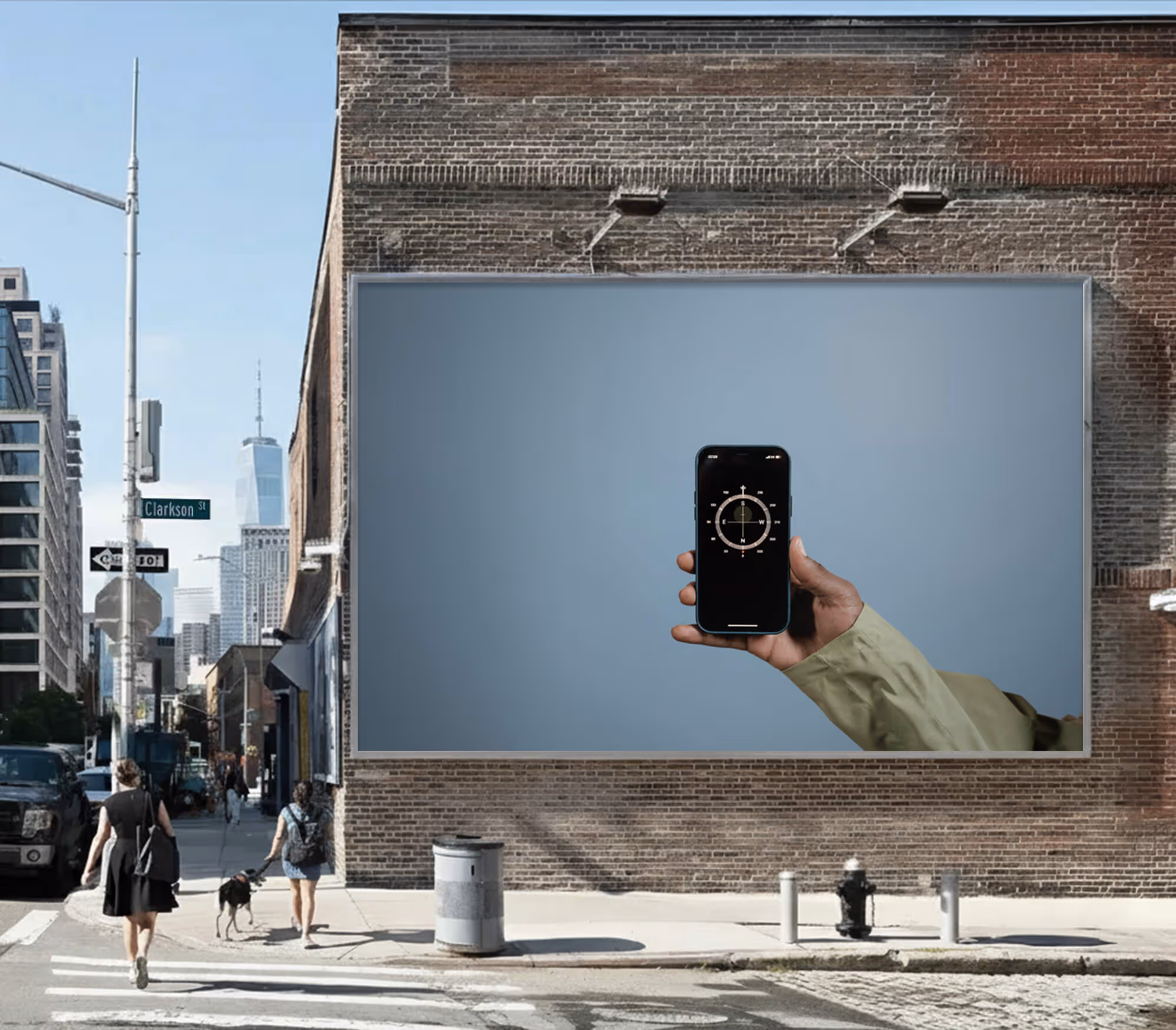 Urban street corner with brick building featuring a large billboard of a hand holding a smartphone displaying a compass app.
