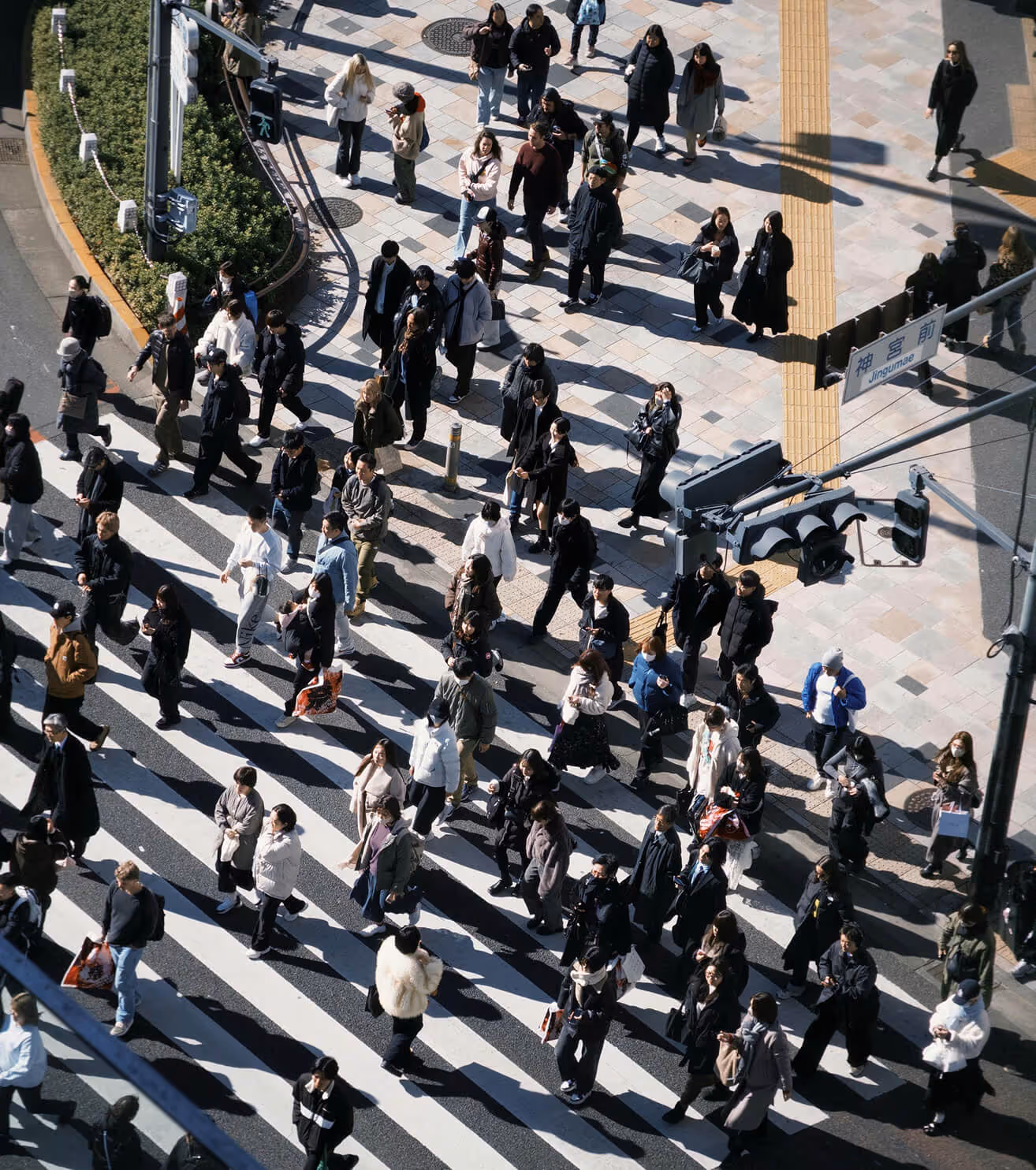 Crowd crossing a wide street at a large pedestrian crosswalk in an urban area on a sunny day.