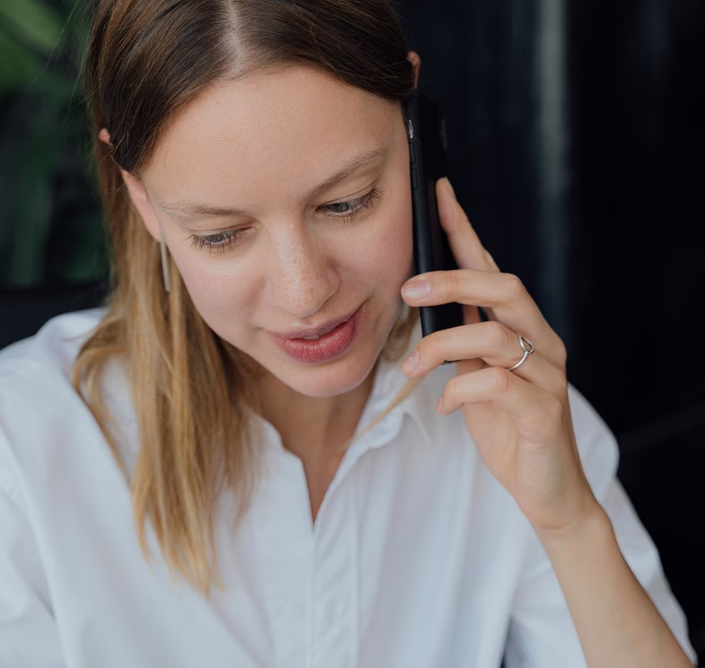 Woman with light brown hair in white shirt talking on a smartphone.