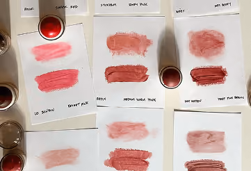 Various lipstick swatches on paper with lipsticks and labels showing shade names and tones.