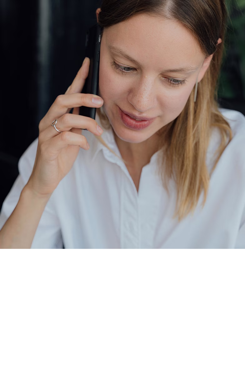 Woman with light brown hair in white shirt talking on a smartphone.