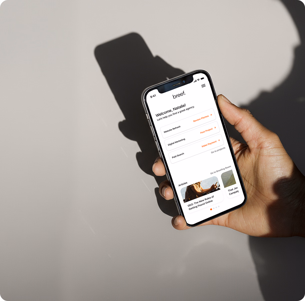 Hand holding a smartphone showing the Breef app dashboard with project options.