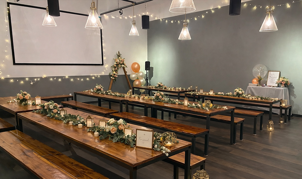 Large event space with projector wall, high ceilings and long tables all decorated with flowers and candles