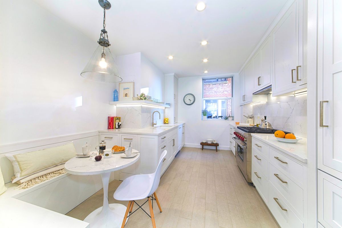 Bright galley kitchen with white cabinetry, brass pulls and a tulip table nook at 895 West End Avenue by Gallery KBNY